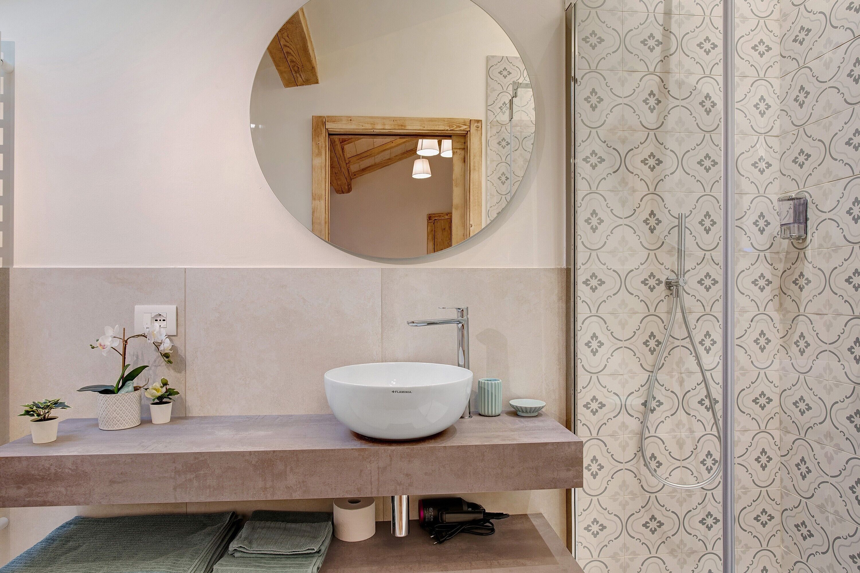 Een badkamer met een ronde spiegel, een wastafel op voet, een douche en betegelde muren.