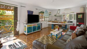 A living room with a sofa, a television, a kitchen area, and a dining table. - Finca Fani 4 with Mountain Views, Shared Pool, Wi-Fi, Terrace & Garden (Agüimes)