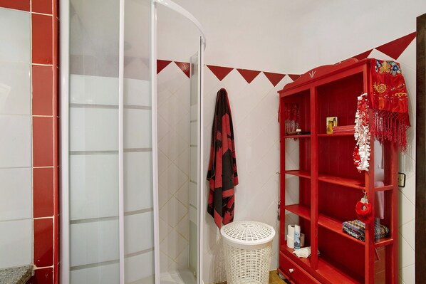 A bathroom with a shower, a red storage unit, and a white laundry basket.