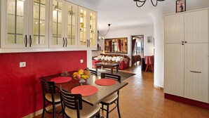 Un coin repas avec un mur rouge, une table en bois et des chaises. On y trouve également une cuisine avec des meubles blancs et un lustre.