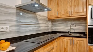 Een moderne keuken met een zwart aanrechtblad, houten kastjes, een roestvrijstalen spoelbak en een inbouw afzuigkap.