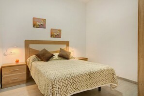 Une chambre à coucher comprenant un lit, deux lampes fixées au mur, une table de chevet avec des tiroirs et deux œuvres d’art murales.