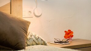 Een slaapkamer met een bed, een nachtkastje met een smartphone, brillen en een bloevas.