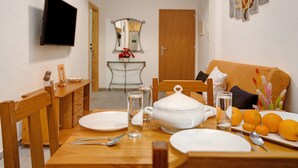 Een eettafel gedekt met borden, bestek, een soepterrine, glazen en sinaasappels, met een aan de muur bevestigde televisie en een spiegel boven de tafel.