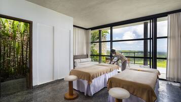 Two single beds with matching headboards and footboards, set in a serene space with a large window offering views of lush greenery.