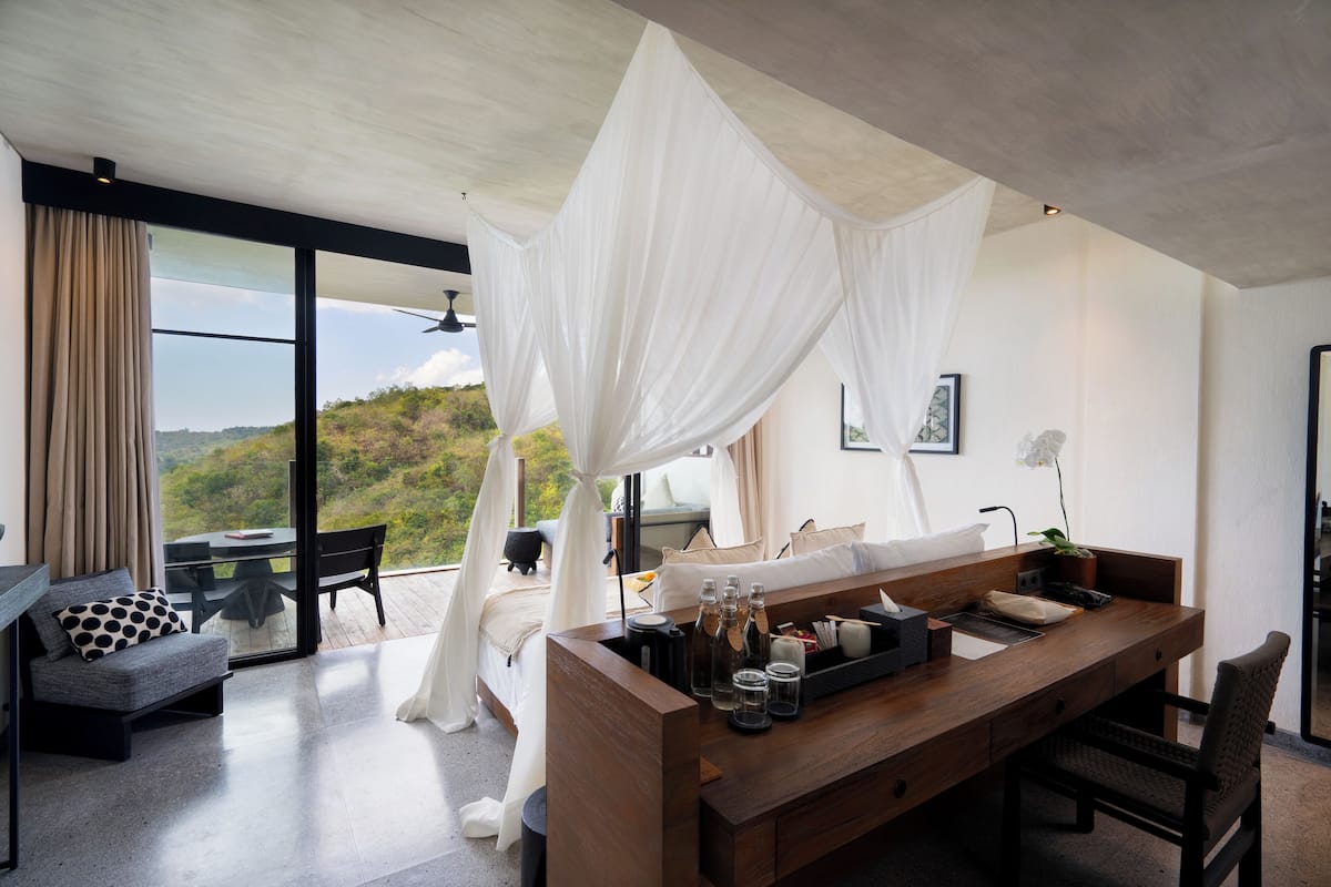 A modern bedroom with a large bed, a wooden desk, and a view of the outdoors.