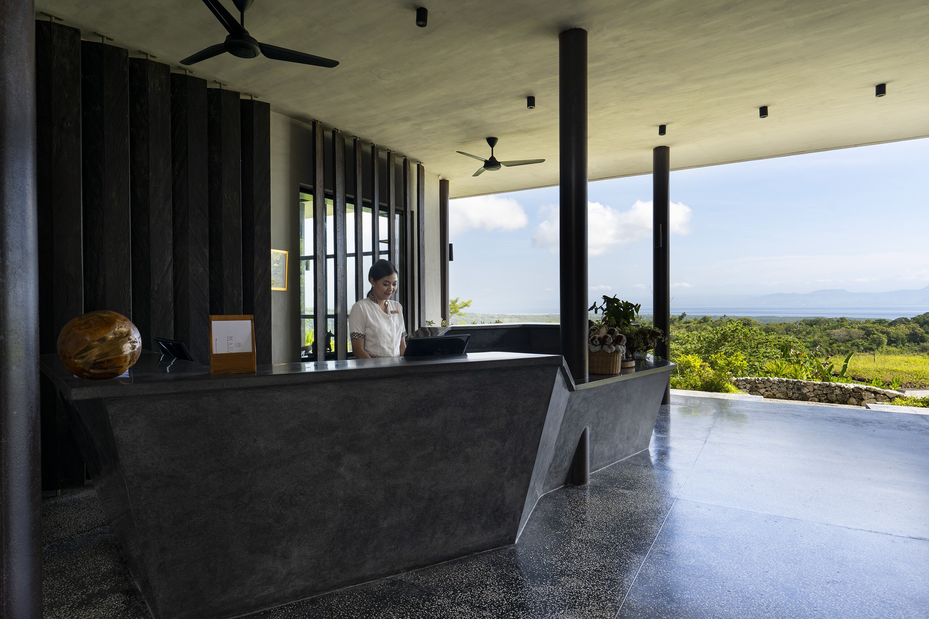A modern reception area with a receptionist, a large decorative vase, and a view of the landscape.
