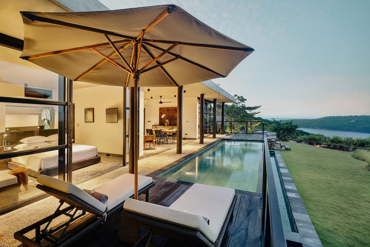 A modern hotel room with a private pool, lounge chairs, and a large umbrella.