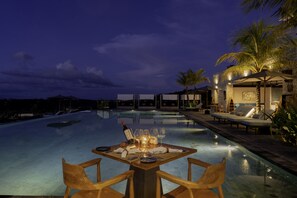 A dining area with a table set for two, overlooking a swimming pool at dusk. - Maua Nusa Penida (Penida Island)