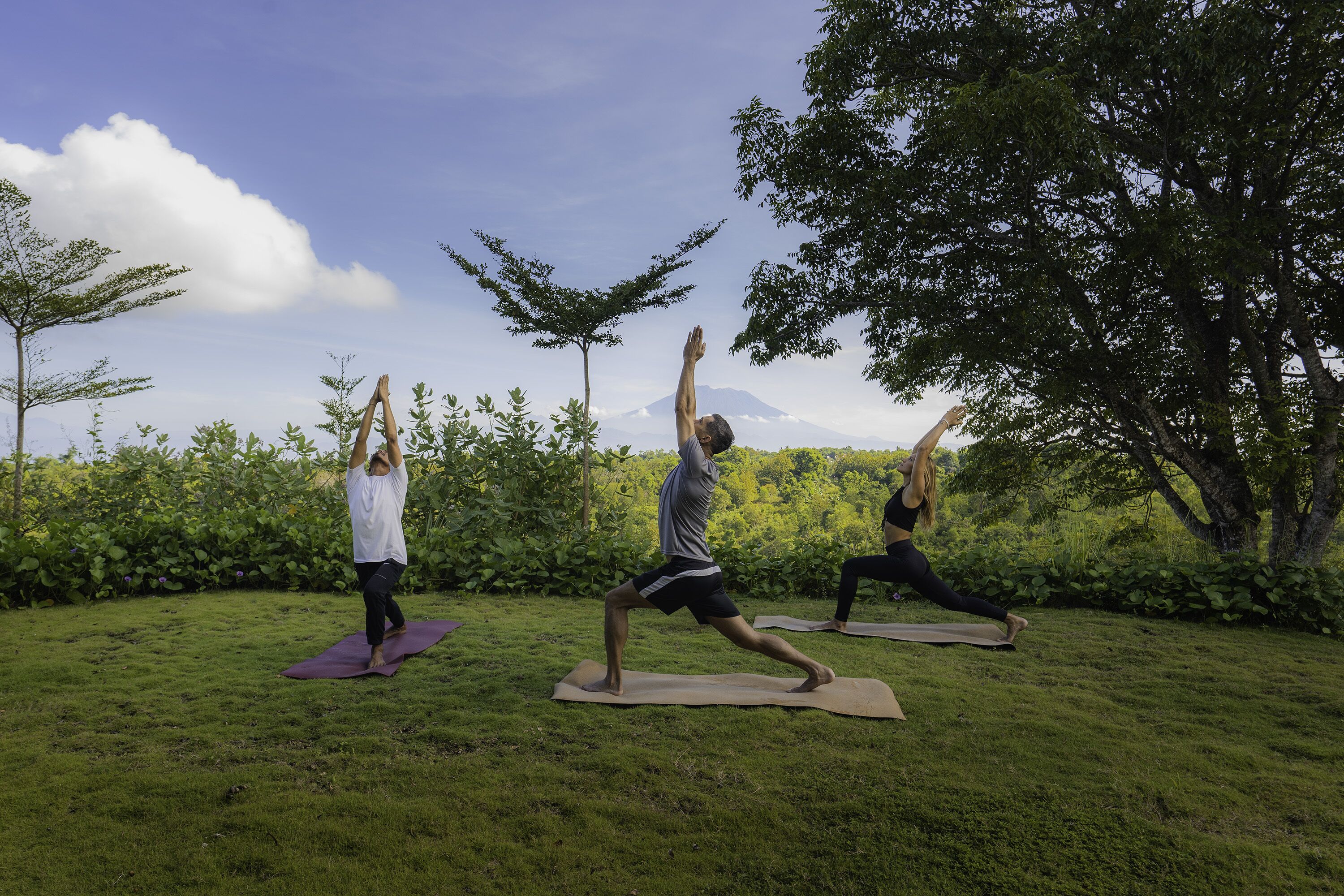 Three people practicing yoga outdoors on mats.