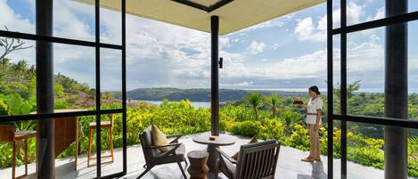 A spacious balcony with a view of a lake and greenery, furnished with chairs and a table.