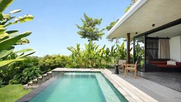 Uma área de piscina moderna ao ar livre com um deck de madeira, cercada por vegetação exuberante e um céu azul límpido.