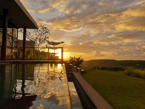 A swimming pool with a sunset view, a stone wall, and a grassy area. - Maua Nusa Penida (Penida Island)