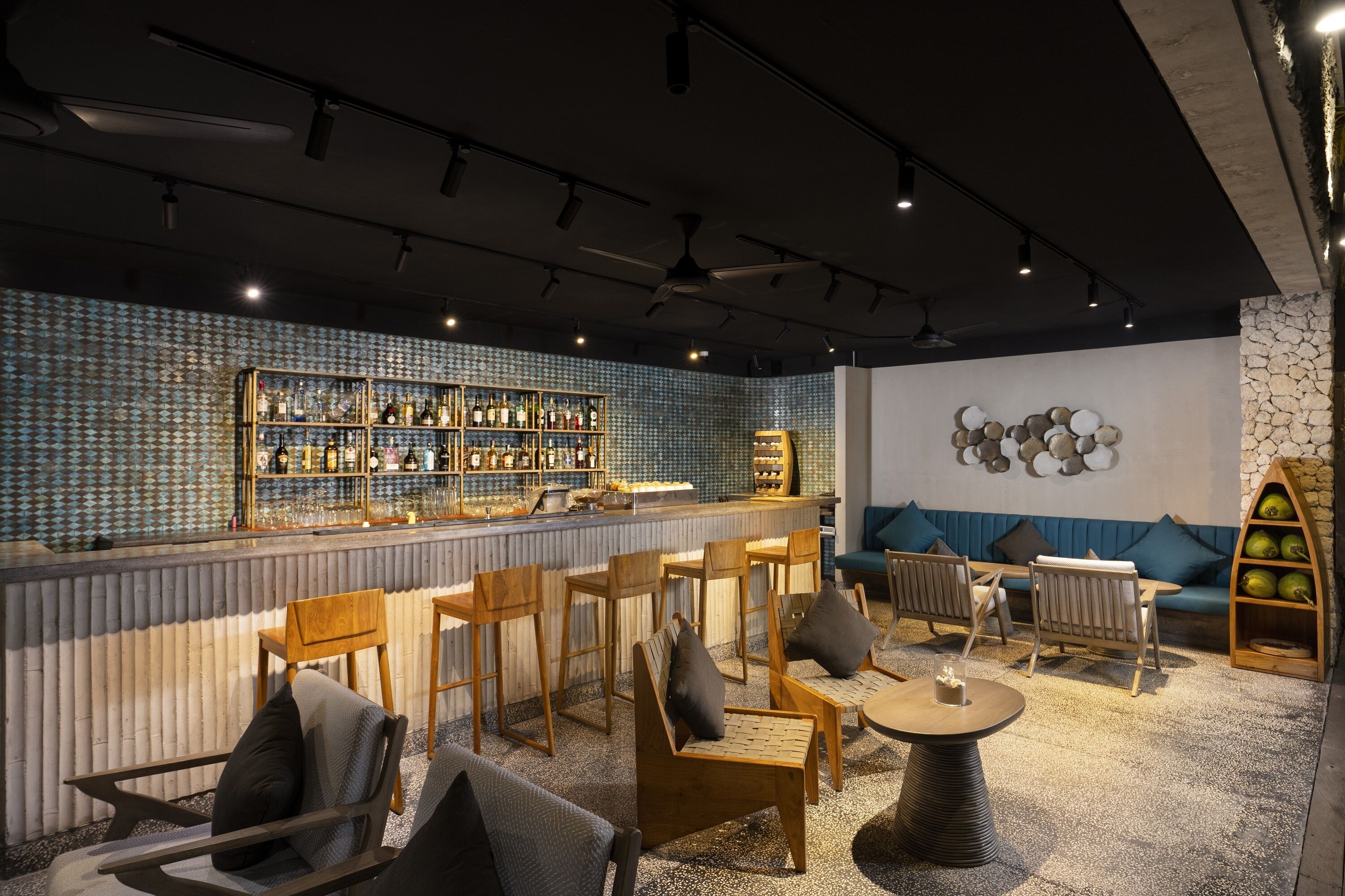 Zona de bar con sillas y mesas de madera, barra con estantes llenos de botellas y pared de piedra con detalles decorativos.