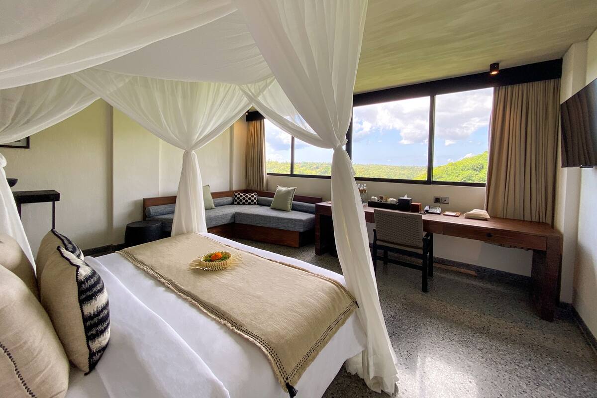 A bedroom with a bed, a desk, and a view of the outdoors.