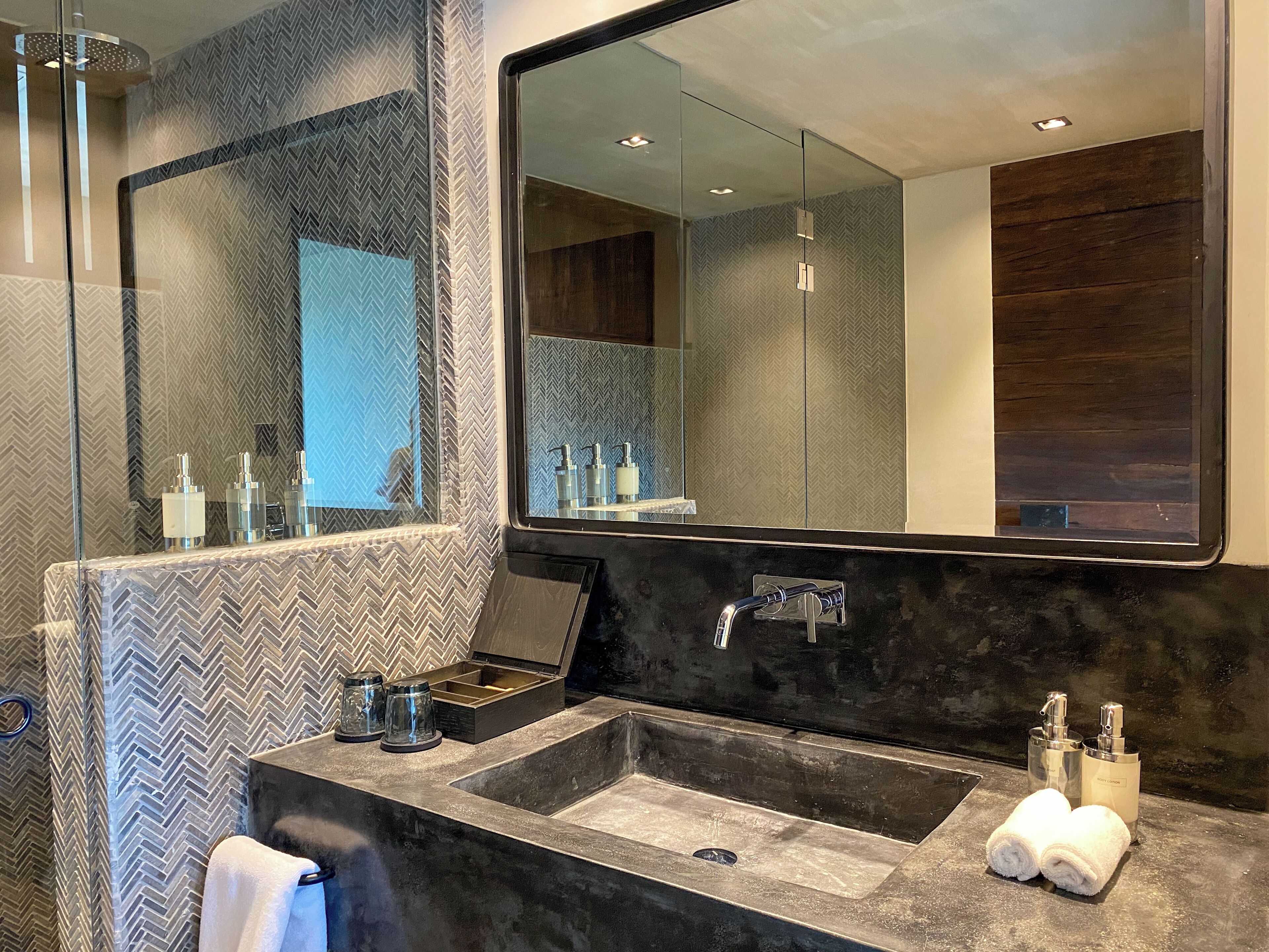 A modern bathroom with a large mirror, two sinks, and a shower.