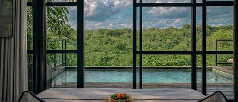 A room with a view of a swimming pool and lush greenery.