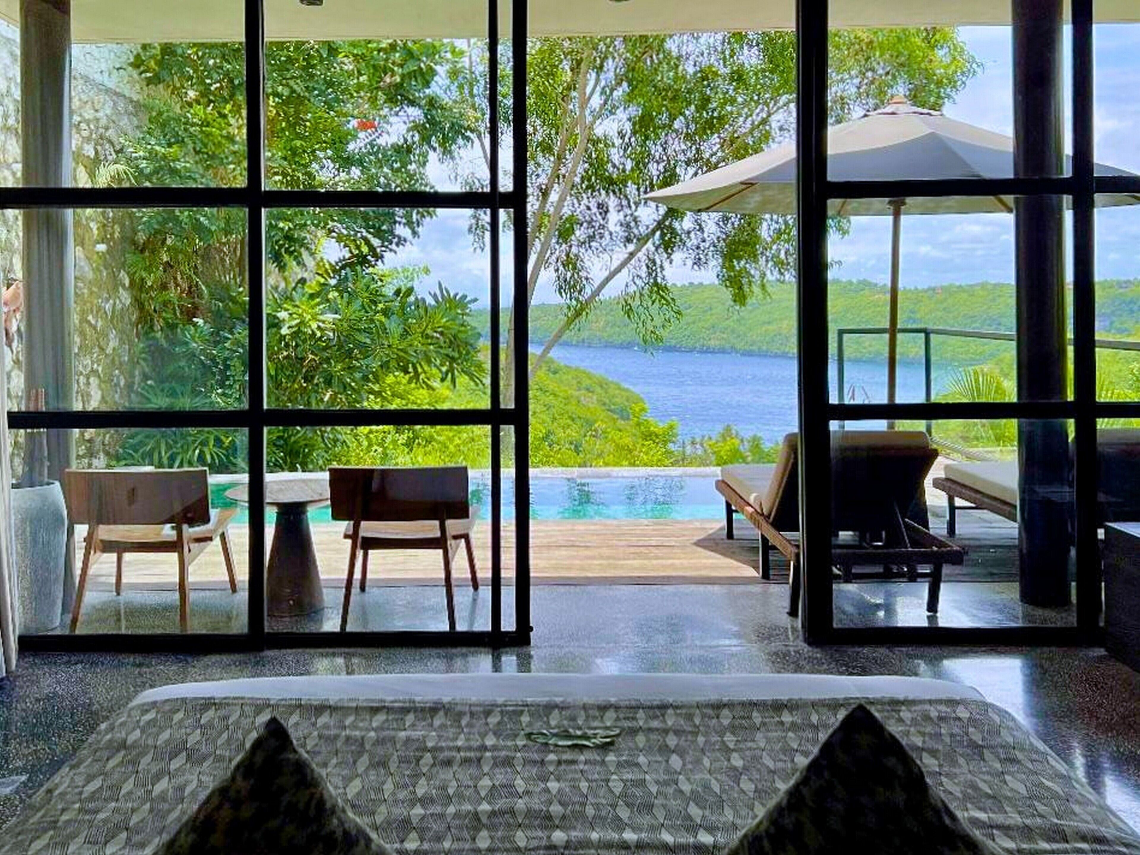 Ein Schlafzimmer mit großem Fenster und Blick auf einen Pool und üppige Grünflächen.