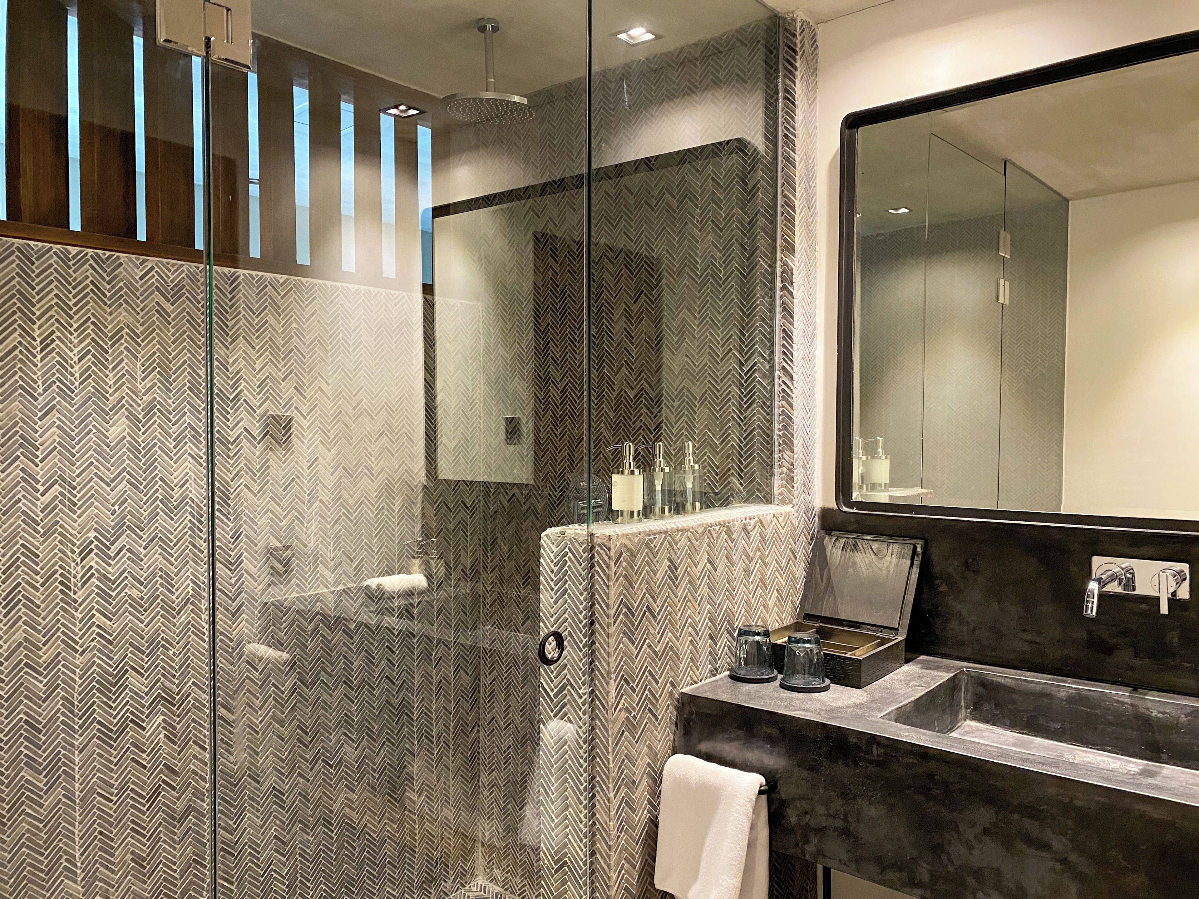 A modern bathroom with a glass shower enclosure, a large mirror, and a marble sink.