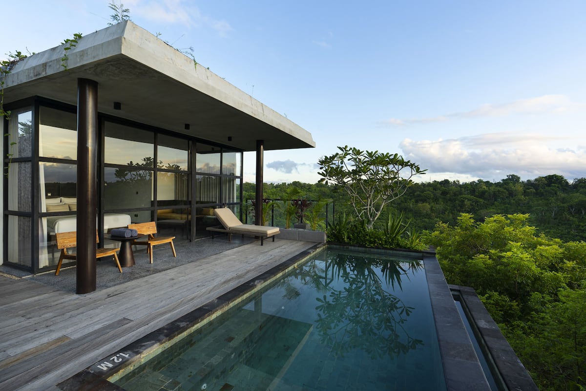 A modern outdoor pool area with a wooden deck, lounge chairs, and a glass-enclosed structure.