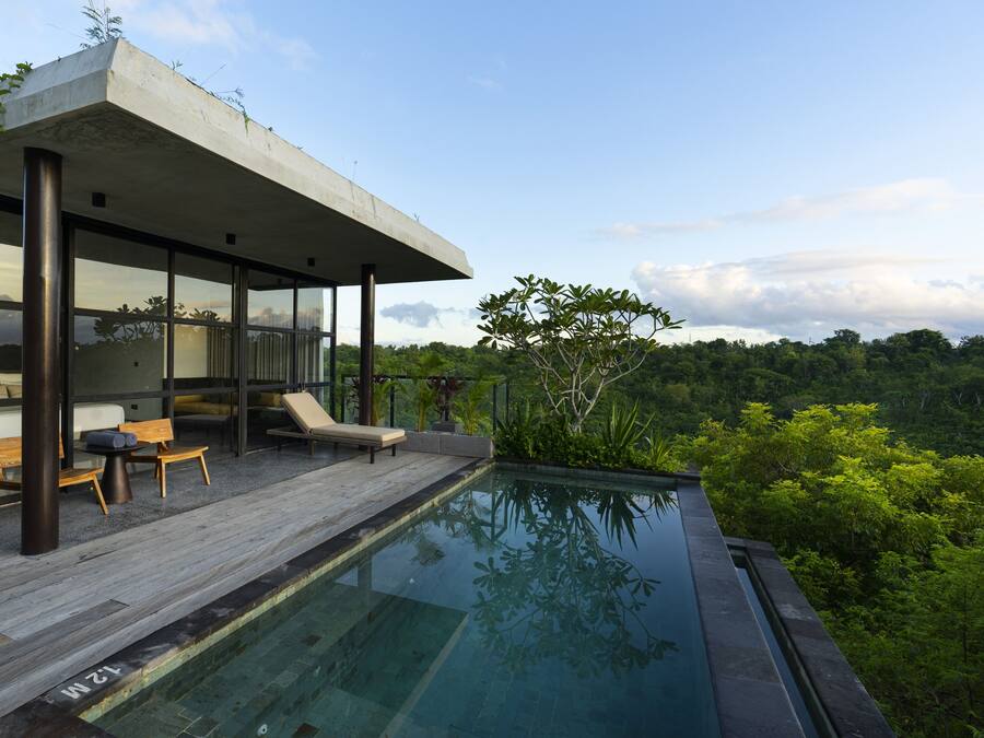 A modern outdoor pool area with a wooden deck, lounge chairs, and a glass-enclosed structure.
