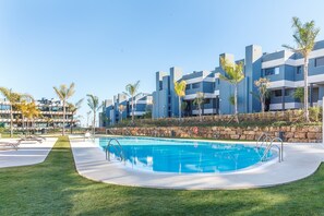 A swimming pool with a stone wall and palm trees, surrounded by modern buildings.