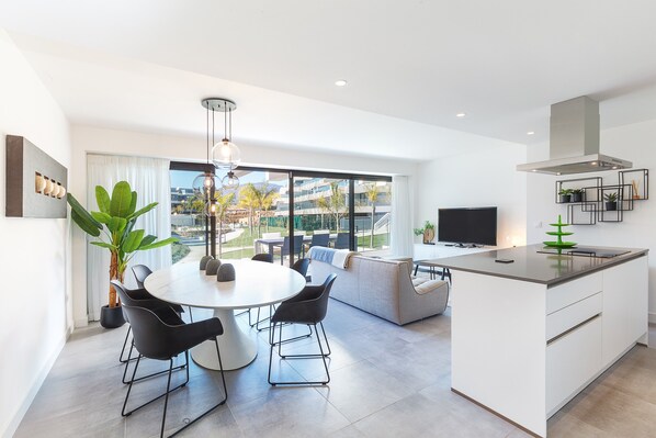 A modern kitchen with a dining area, large windows, and a view of the outdoors.