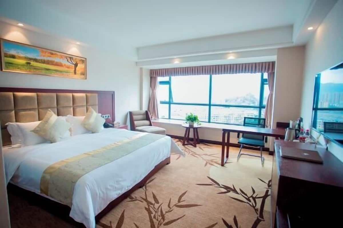 A hotel room with a large bed, a desk, a chair, a television, and a window with a view.