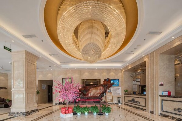 Un vestíbulo de hotel con una gran araña, una recepción y una escultura decorativa.