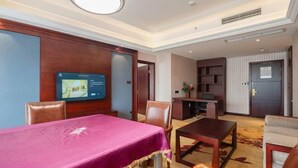 Una habitación de hotel con una mesa de comedor, sillas, un televisor, una estantería y una puerta.