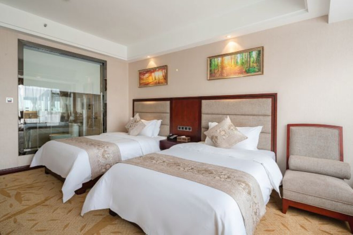 A hotel room with two beds, a chair, and artwork on the walls.