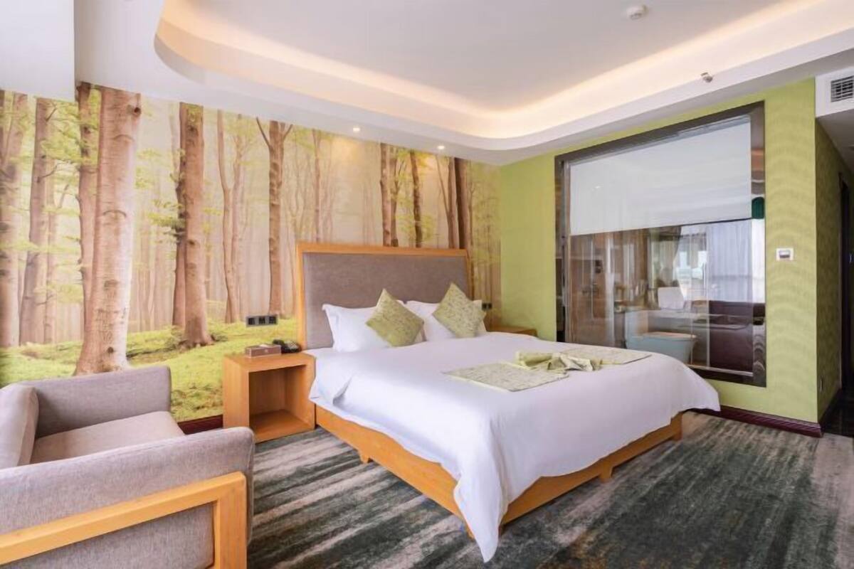 A hotel room with a large bed, a nightstand, a chair, and a forest-themed wall mural.