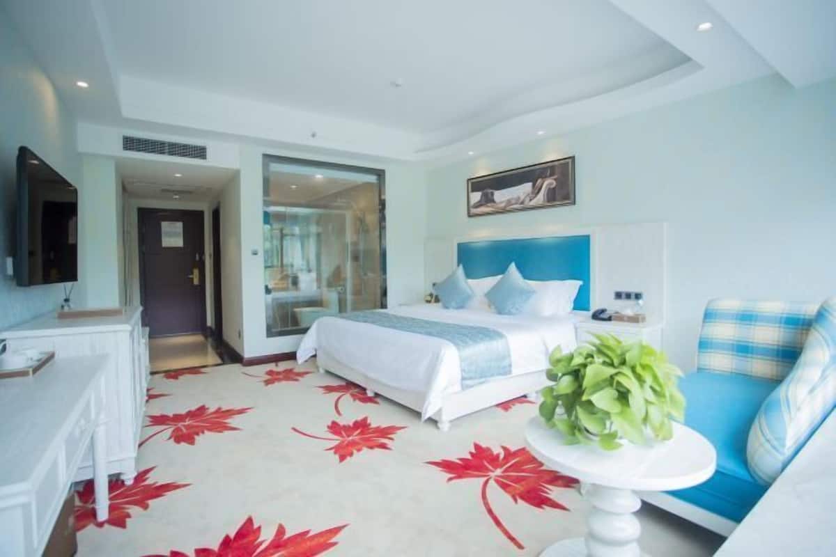 A modern hotel room with a bed, a desk, a chair, and a small table with a plant.