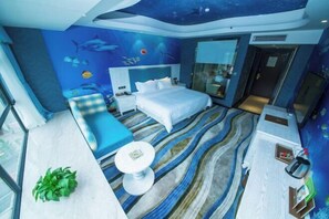 A modern hotel room with a large bed, a seating area, a small table, and a view of the ocean through the windows. - Yuhe Hotel (Leshan)