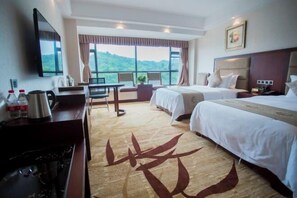A hotel room with two beds, a desk with a chair, a TV, and a large window offering a view of greenery. - Yuhe Hotel (Leshan)