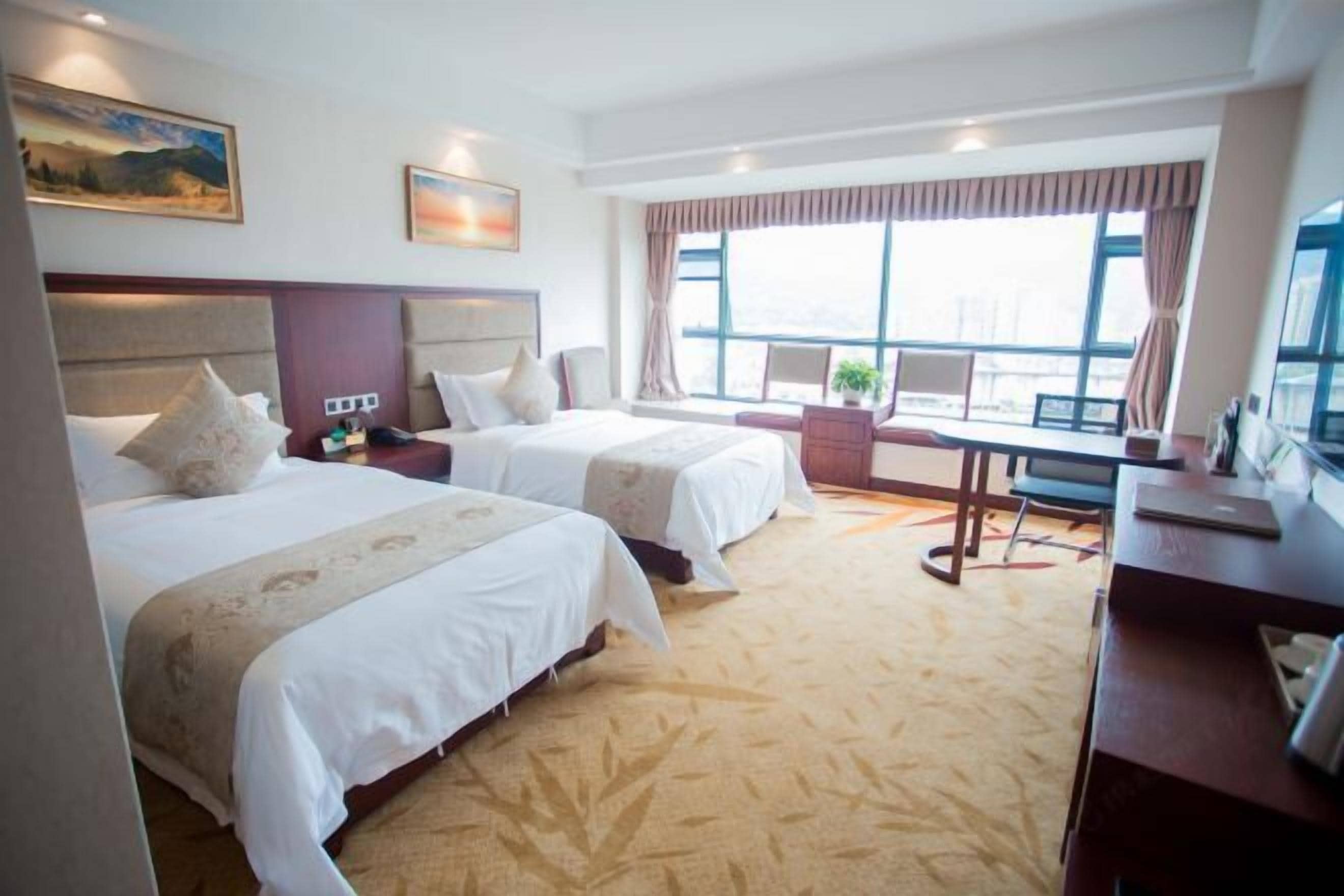 A hotel room with two beds, a desk, and a large window with curtains.
