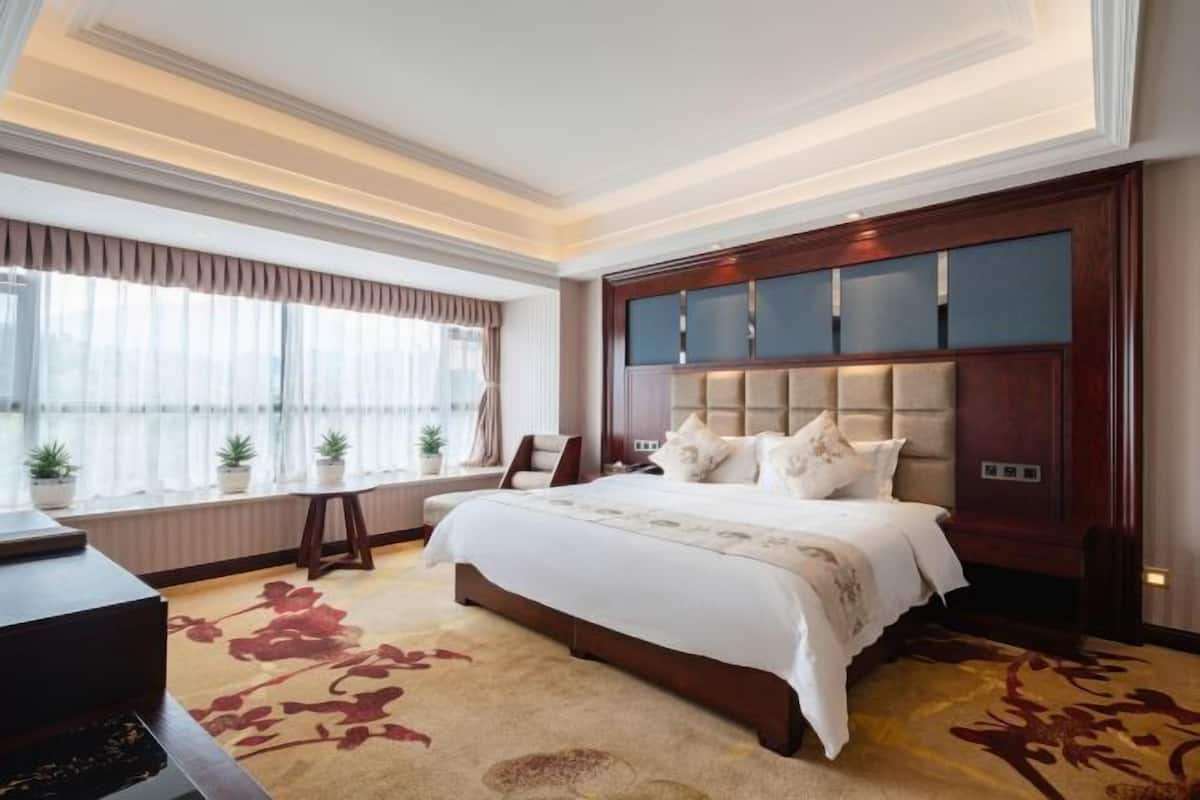 A spacious bedroom with a large bed, a wooden headboard, and a view of the city through large windows.