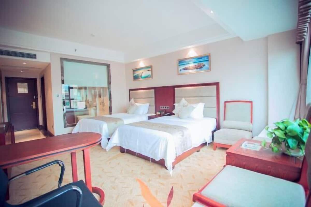 A hotel room with two beds, a desk, a chair, and a small table with a plant.