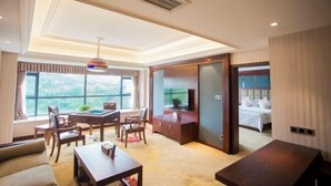 Una habitación de hotel moderna con un ventanal grande, una zona de comedor con mesa de billar, un sofá y un televisor.