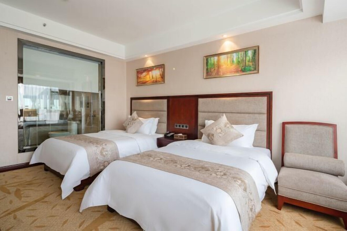 A hotel room with two beds, a chair, and artwork on the walls.