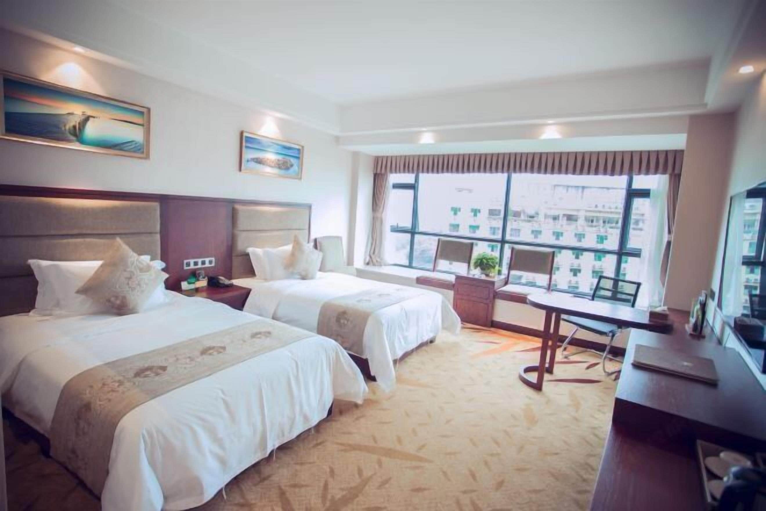 A hotel room with two beds, a desk, a chair, and a large window with a city view.