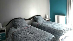 A bedroom with two beds, a white nightstand, a white lamp, and a radiator. - Family home in the country (groslee saint benoit)
