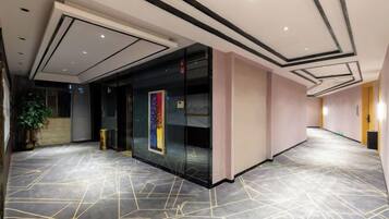 A spacious hallway with a geometric patterned floor, a glass wall with a colorful artwork, and a modern ceiling design.