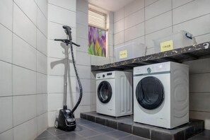 A laundry area with a vacuum cleaner, two washing machines, and a shelf with containers. - ShangPing xifeng Hotel (Xinfeng)