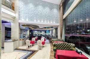 Un amplio vestíbulo de hotel con techo alto, zona de bar central y diferentes distribuciones de asientos.