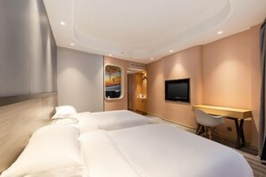 Ein Hotelzimmer mit zwei Betten, einem Schreibtisch, einem Fernseher und einem Fenster mit Blick auf einen Sonnenuntergang.