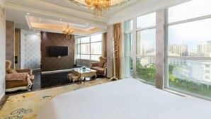 Habitación de hotel con una cama grande, televisión, candelabro, sofá y vistas de la ciudad.