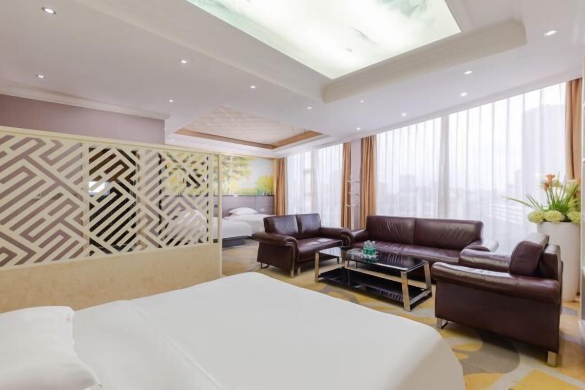 Ein Hotelzimmer mit einem großen Bett, zwei Ledersofas, einem Couchtisch und einem dekorativen Raumteiler.