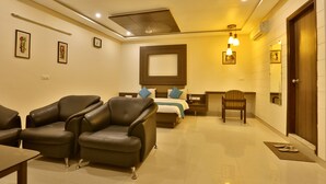 Una habitación de hotel con una cama, dos sillones de cuero, una mesita y una mesita de noche con una lámpara.