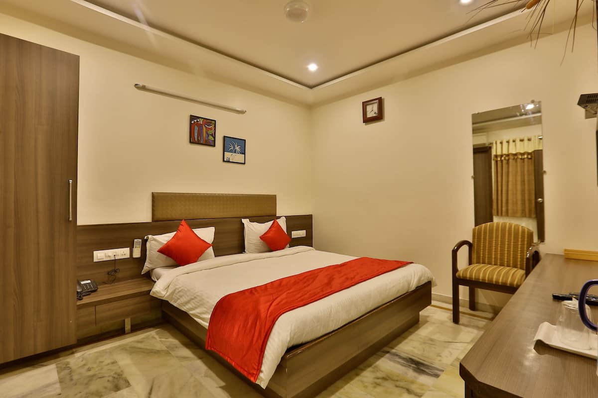 A hotel room with a large bed, a wooden wardrobe, a bedside table with a phone, and a chair.